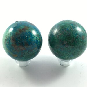 May include: Two green and brown gemstone spheres on clear stands. The spheres are polished and have a marbled appearance.
