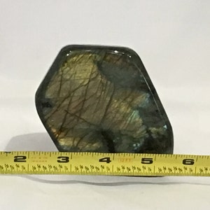 May include: A large, irregularly shaped piece of labradorite with a dark green, blue, and gold iridescent sheen. The stone is approximately 4 inches wide.