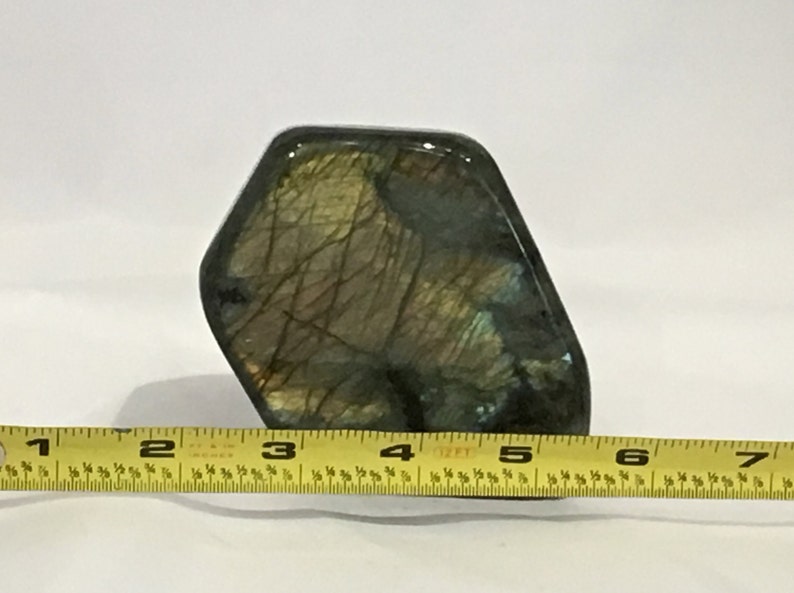 May include: A large, irregularly shaped piece of labradorite with a dark green, blue, and gold iridescent sheen. The stone is approximately 4 inches wide.