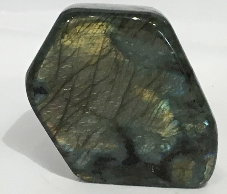 May include: A large, dark green, iridescent labradorite gemstone with a hexagonal shape. The stone has a smooth, polished surface and displays a variety of colors, including blue, green, and gold.