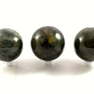 May include: Three dark green labradorite spheres on clear stands. The spheres are polished and have a iridescent sheen.