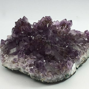 May include: A large amethyst cluster with many purple crystals on a natural rock base.