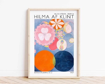 Puede incluir: Una impresión enmarcada de una pintura abstracta colorida de Hilma af Klint titulada "Barnåldern, Nr. 2" de 1907. La pintura presenta un fondo azul con círculos superpuestos en tonos de rosa, naranja, amarillo y azul.