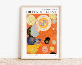 Puede incluir: Una impresión enmarcada de una pintura abstracta de Hilma af Klint titulada "Inglingaaldren, No. 3" de 1907. La pintura presenta una composición colorida de círculos, espirales y líneas sobre un fondo rojo.