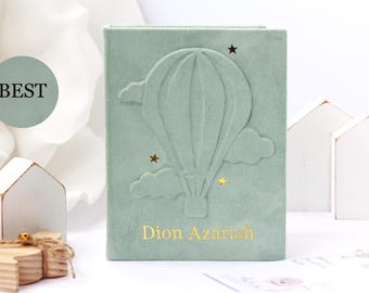 May include: A sage green velvet-textured notebook featuring an embossed hot air balloon design surrounded by clouds and small gold stars. The name Dion Azariah is printed in gold lettering at the bottom center of the front cover.