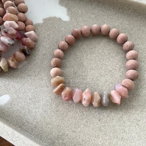 May include: A pink and white gemstone bracelet with wooden beads. The bracelet is made with natural stones and is a beautiful and unique piece of jewelry.
