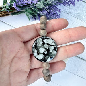 May include: A wooden bead bracelet featuring a large, round, black and white marbled pendant. The pendant has a white background with black swirls and spots.