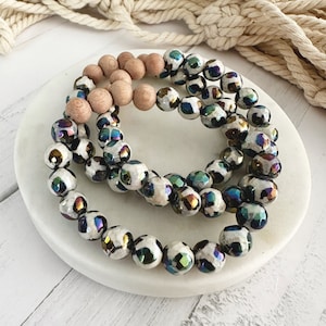 May include: Two bracelets made of iridescent, white, and black patterned beads. One bracelet is made of wooden beads.