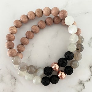 Op de afbeelding: Een gelaagde armband met houten, witte, grijze, zwarte en roségouden kralen.