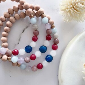 May include: Three layered bracelets with wooden beads and gemstone beads in shades of blue, pink and red.