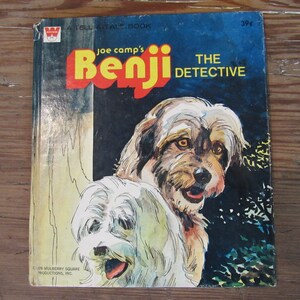 May include: A vintage children's book cover featuring a cartoon illustration of two dogs. The book is titled "Joe camp's Benji The Detective" and is a "Tell A Tale Book".