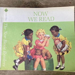 May include: A vintage softcover book titled Now We Read, The New Basic Readers, Teacher's Edition. The cover features three children playing with a tin can telephone, wearing yellow and pink dresses, with a teddy bear and two rag dolls.