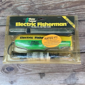 May include: A packaged Electric Fisherman fillet knife set by Mister Twister. The package includes a green and yellow electric knife with a black cord, and a silver blade. The packaging has text that reads "The fastest way to clean a fish."