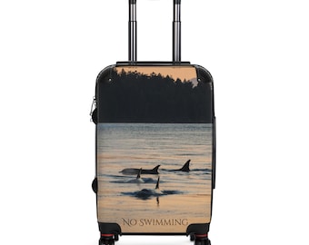 May include: A rolling suitcase featuring a scenic image of orcas swimming in the ocean at sunset. The image includes the text "NO SWIMMING" at the bottom. The suitcase has a black handle and wheels.
