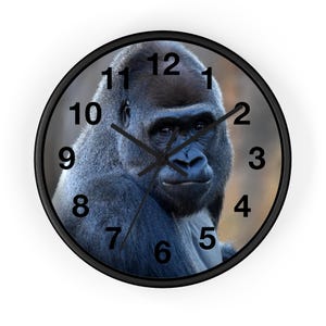 Puede incluir: Un reloj de pared blanco y negro con una cara de gorila en el centro. Los números del 1 al 12 están alrededor del borde de la esfera del reloj.