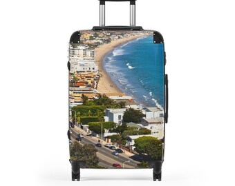 May include: A rolling suitcase featuring a vibrant coastal scene. The design showcases a beach with blue ocean waves, a sandy shore, and buildings along the coast. The suitcase has a black handle and wheels, perfect for travel.