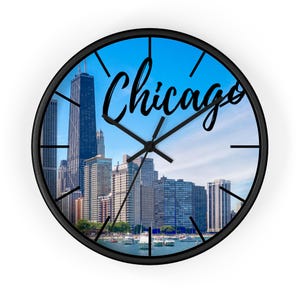 May include: A black and white clock with a cityscape of Chicago, Illinois. The clock face features a blue sky with white clouds and the word "Chicago" in a black cursive font.
