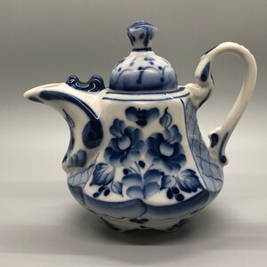 Könnte beinhalten: Eine kleine, weiße Porzellan-Teekanne mit einem blauen und weißen Blumenmuster. Die Teekanne hat einen Deckel und einen Henkel.
