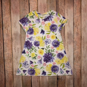 May include: A white dress with a floral print featuring yellow and purple flowers. The dress has short sleeves and a round neckline.