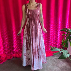 May include: A sleeveless floor-length dress featuring a white base color with a dark red vertical drip pattern that resembles paint streaks. The garment has a square neckline and a fitted bodice that flows into a wider skirt at the hemline.