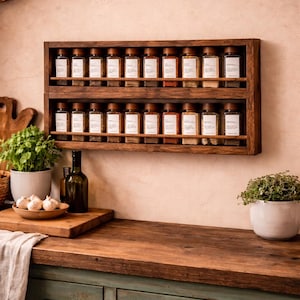 May include: A wall-mounted wooden spice rack featuring two horizontal shelves. Each shelf holds ten clear glass spice jars with dark wooden lids and white rectangular labels. The rack is constructed from dark brown wood with a simple, open-front design.