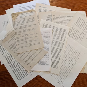 May include: A pile of papers with text in various languages, including English, French, German, and Japanese. The papers are on a wooden surface.