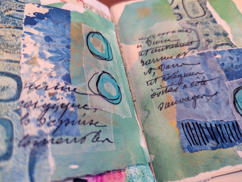 May include: An open journal page with mixed media art. The artwork features layered paper with watercolor washes in shades of blue and green. Handwritten script and abstract shapes are visible.