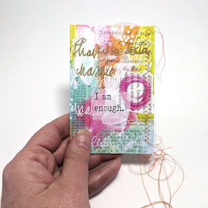May include: A colorful, abstract art piece with the text "I am enough." The art piece is made of paper and fabric and has a hand-stitched edge.