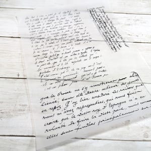 May include: A translucent sheet of paper with handwritten text in black ink. The script appears to be in a cursive style, with some areas of the text overlapping. The paper is placed on a white wooden surface.