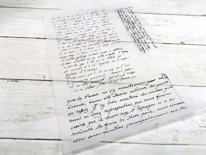 May include: A translucent sheet of paper with handwritten text in black ink. The script appears to be in a cursive style, with some areas of the text overlapping. The paper is placed on a white wooden surface.