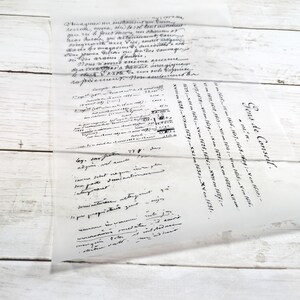 May include: A translucent sheet of paper with handwritten text in black ink. The paper is slightly crumpled and lies on a white wooden surface. The text appears to be in a script style, with some areas more densely written than others.