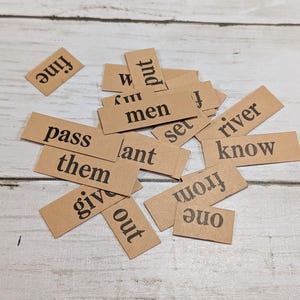 May include: A collection of small, rectangular tan paper word tiles featuring black printed text. The visible words include fine, put, my, men, set, river, pass, lant, them, know, give, out, from, and one, scattered in a random arrangement.