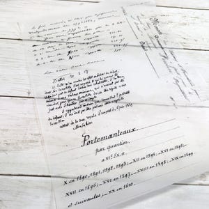 May include: A translucent sheet of paper with handwritten text in black ink, featuring the word "Portemanteaux" and dates like "1590" and "1610." The paper is laid on a white wooden surface.