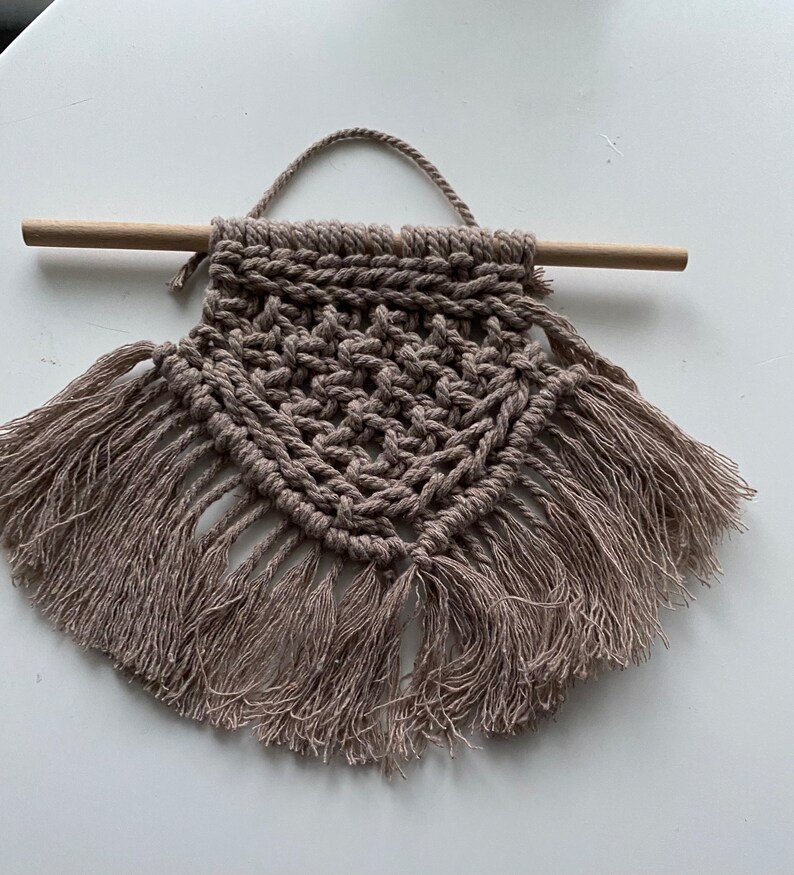 Może przedstawiać: Beżowy wiszący makramowy z drewnianym drążkiem i frędzlami.