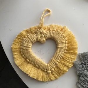 Może przedstawiać: Ż&oacute;łty wiszący makramowy w kształcie serca z frędzlami.