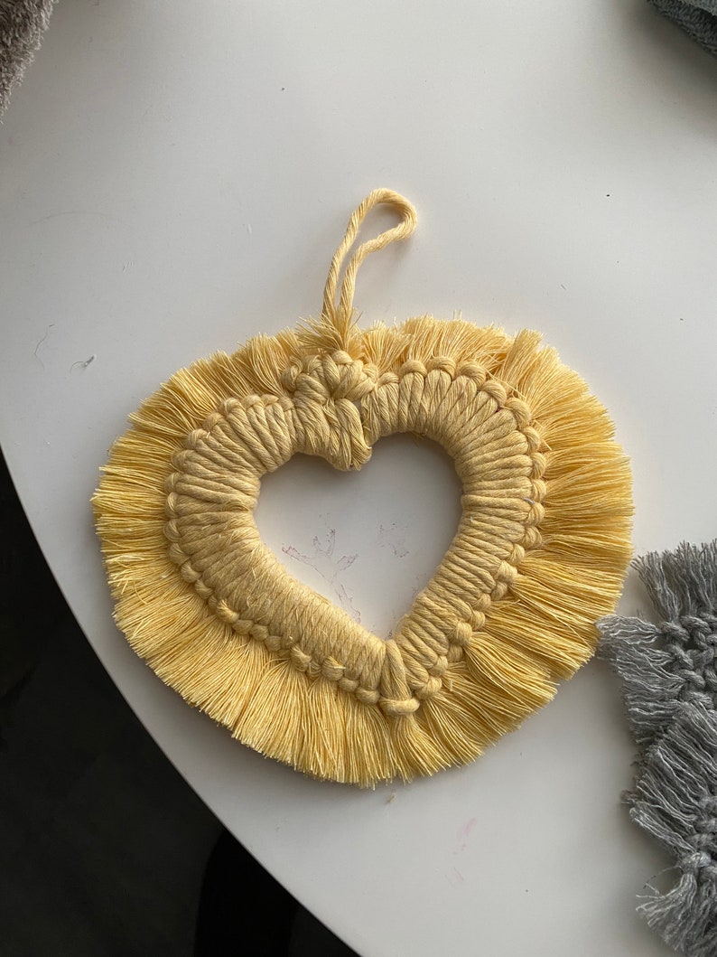 Może przedstawiać: Ż&oacute;łty wiszący makramowy w kształcie serca z frędzlami.