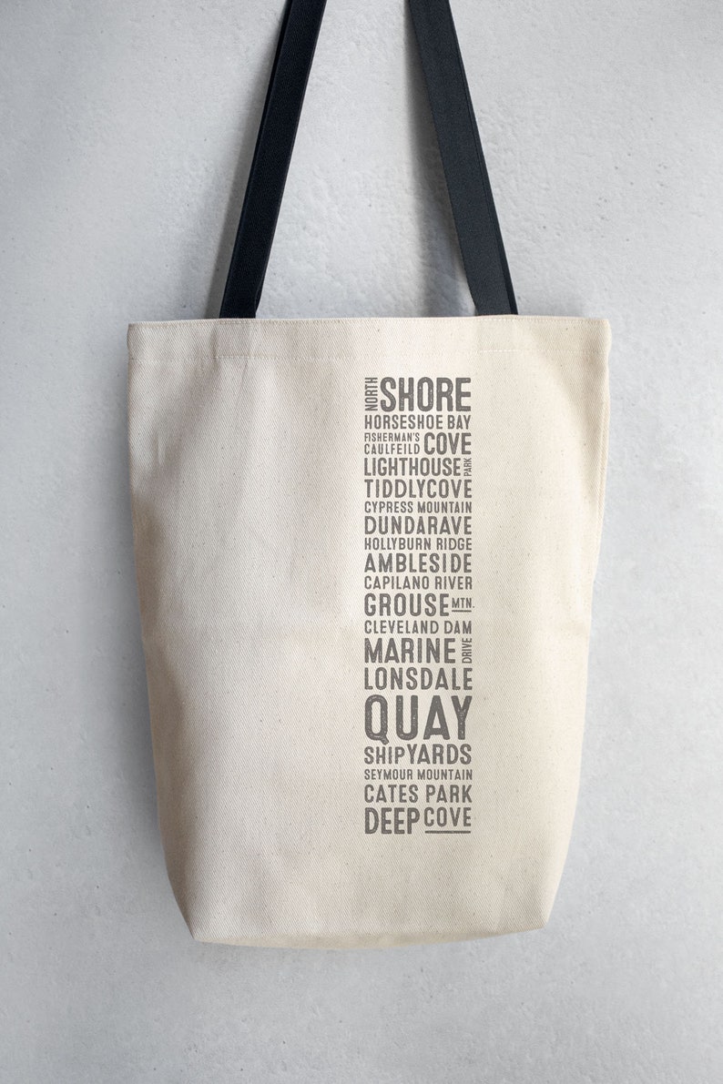 Puede incluir: Una bolsa de lona blanca con correas negras. La bolsa presenta una lista vertical de puntos de referencia de North Shore, Columbia Brit&aacute;nica, que incluyen Horseshoe Bay, Caulfeild Cove, Lighthouse, Tiddy Cove, Cypress Mountain, Dundarave, Hollyburn Ridge, Ambleside, Capilano River, Grouse Mountain, Cleveland Dam, Marine Drive, Lonsdale, Quay, Shipyards, Seymour Mountain, Cates Park y Deep Cove.