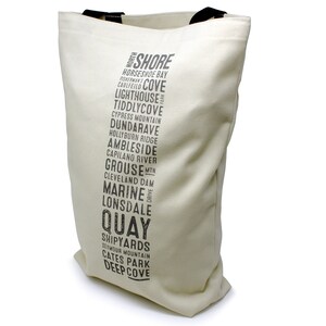 Puede incluir: Una bolsa de lona blanca con texto negro que enumera varios lugares en North Shore, Columbia Brit&aacute;nica. El texto dice "North Shore", "Horseshoe Bay", "Cholfield", "Lighthouse", "Tiddlycove", "Cypress Mountain", "Dundarave", "Hollyburn Ridge", "Ambleside", "Capilano River", "Grouse Min", "Cleveland Dam", "Marine Drive", "Lonsdale", "Quay", "Shipyards", "Seymour Mountain", "Cates Park" y "Deep Cove".