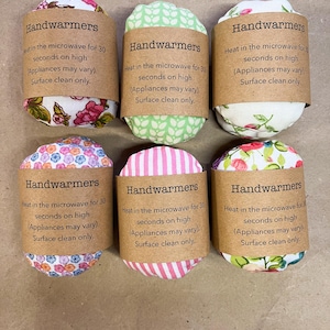 May include: Six hand warmers with fabric covers in various floral and patterned designs. Each warmer has a brown label with the text "Handwarmers" and instructions for microwave use. Surface clean only.