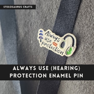 May include: Gold enamel pin with the text "Always use protection" and a stylized image of headphones. The pin is on a black lanyard.