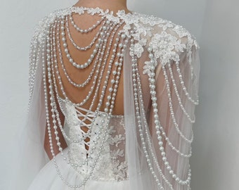 Puede incluir: Un vestido de novia blanco con falda de tul y corpiño de encaje. El vestido presenta un adorno de perlas y cadenas en la espalda, creando un look dramático y elegante. El vestido está etiquetado como "Sherbon".