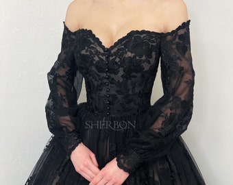 May include: Black off-the-shoulder gown with long, sheer sleeves. The bodice features intricate floral lace detailing and a row of small buttons. The skirt is layered with tulle, creating a full silhouette. The brand name "SHERBON" is visible.