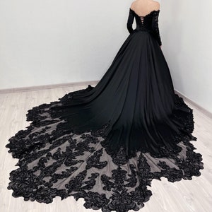 Peut inclure: Une robe noire à épaules dénudées avec des manches longues et une traîne en dentelle. La robe a un corsage ajusté et une jupe ample.