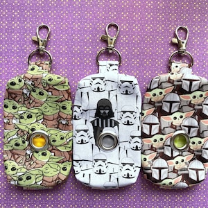 Puede incluir: Tres llaveros de tela con diferentes dise&ntilde;os de personajes de Star Wars. El llavero de la izquierda presenta un patr&oacute;n repetido de personajes de Baby Yoda. El llavero del medio presenta un patr&oacute;n repetido de personajes de Stormtrooper y Darth Vader. El llavero de la derecha presenta un patr&oacute;n repetido de personajes de Baby Yoda y Mandalorian.