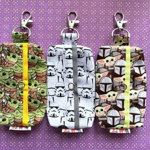 Puede incluir: Tres llaveros de tela con diferentes dise&ntilde;os de personajes de Star Wars. El llavero de la izquierda presenta un patr&oacute;n repetido de Baby Yoda, el llavero del medio presenta un patr&oacute;n repetido de Stormtroopers y el llavero de la derecha presenta un patr&oacute;n repetido de personajes mandalorianos.