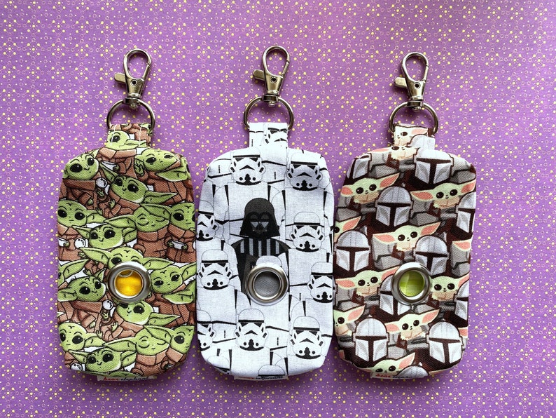 Puede incluir: Tres llaveros de tela con diferentes dise&ntilde;os de personajes de Star Wars. El llavero de la izquierda presenta un patr&oacute;n repetido de personajes de Baby Yoda. El llavero del medio presenta un patr&oacute;n repetido de personajes de Stormtrooper y Darth Vader. El llavero de la derecha presenta un patr&oacute;n repetido de personajes de Baby Yoda y Mandalorian.