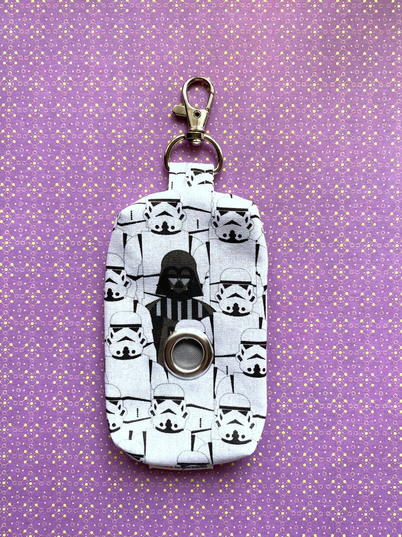 Puede incluir: Porta bolsas de caca de tela blanca con un estampado de Star Wars en blanco y negro con Darth Vader y Stormtroopers. El porta bolsas tiene un clip plateado y un ojal plateado.