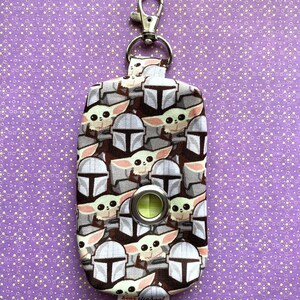 Puede incluir: Una peque&ntilde;a bolsa de tela negra y blanca con un clip plateado. La bolsa tiene un patr&oacute;n repetido de un personaje de dibujos animados con ojos grandes y una boca peque&ntilde;a. La bolsa tiene un anillo de pl&aacute;stico verde en la parte delantera. La bolsa tiene una etiqueta que dice "bear elephant".