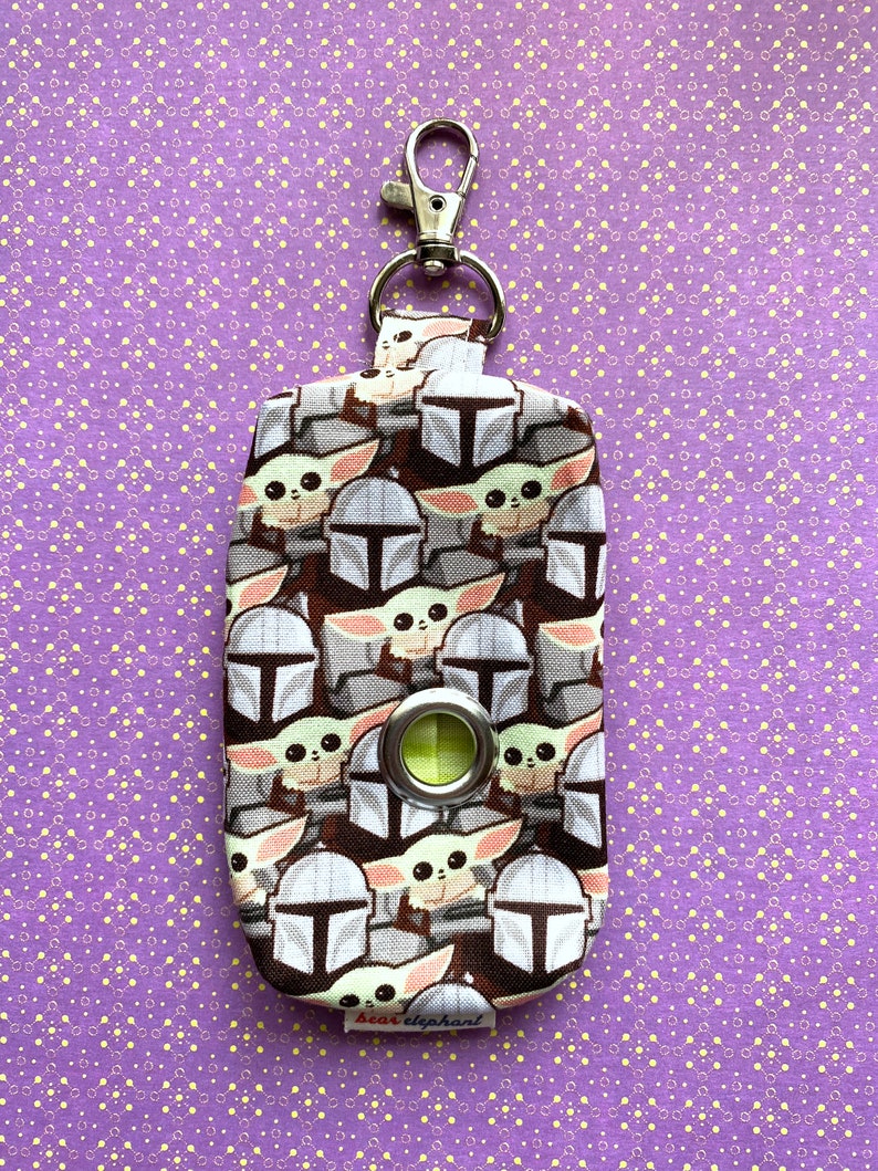 Puede incluir: Una peque&ntilde;a bolsa de tela negra y blanca con un clip plateado. La bolsa tiene un patr&oacute;n repetido de un personaje de dibujos animados con ojos grandes y una boca peque&ntilde;a. La bolsa tiene un anillo de pl&aacute;stico verde en la parte delantera. La bolsa tiene una etiqueta que dice "bear elephant".