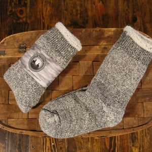 May include: Two pairs of grey wool socks with white trim. The socks are folded and displayed on a wooden surface.